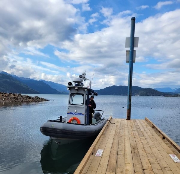 A police boat with a member onboard is moored to a dock on Harrison Lake