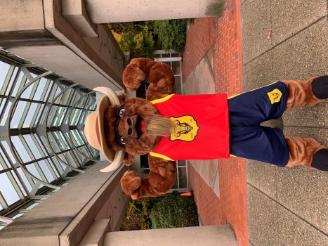 Une mascotte de bison en uniforme de basketball portant un maillot de basketball rouge de la GRC, des shorts de basketball bleus et un chapeau Stetson brun devant l’immeuble du Détachement de la GRC de Surrey.