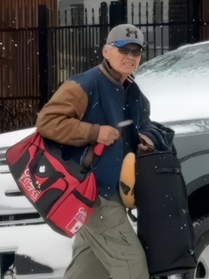 Photo of the suspect wearing a blue and tan bomber jacket, green cargo pants, a grey ball cap and sunglasses