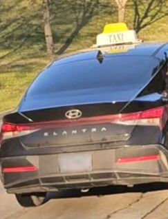 A black sedan with a yellow and white taxi sign on its roof outside 