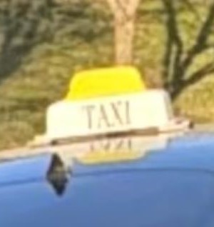 A closeup image of a yellow and white taxi sign on top of a dark vehicle’s roof