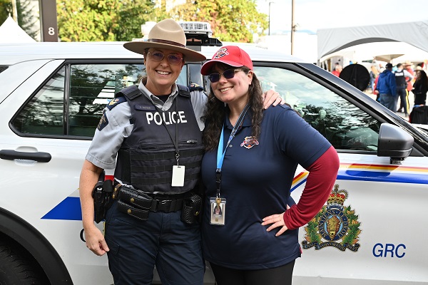 Une gendarme portant un chapeau Stetson se tient à côté d’une employée de la GRC, les deux devant un véhicule de police de la GRC
