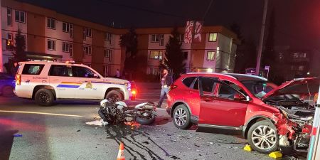 A damaged red SUV and damaged motorcycle on its side on a street at night