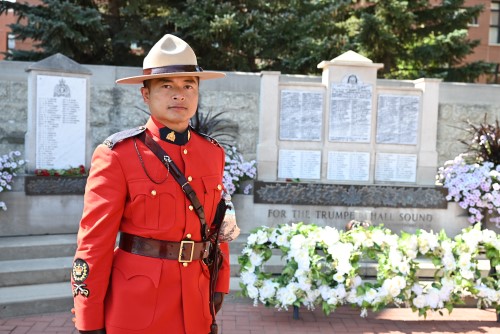 Staff Sgt. Major David Douangchanh, dressed in Red Serge, stands by an RCMP memorial with the names of fallen officers on a sunny day in Regina.