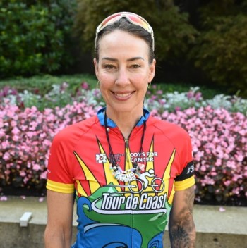 Sgt. Tess Landry (Ret) stands in cycling attire in front of flowers at Burnaby City Hall. 