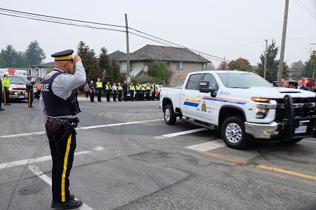 Image of RCMP officer in uniform saluting as an RCMP vehicle drives by