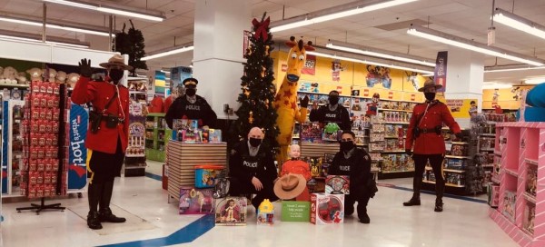 Five police officers wearing uniforms stand in a toy store near a Christmas tree with toys in front of them