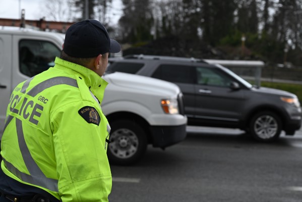 A police officer in a jacket and hat stands beside traffic
