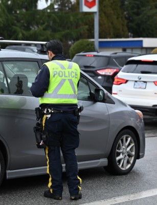 A police officer wearing a reflective jacket stands beside a vehicle in traffic