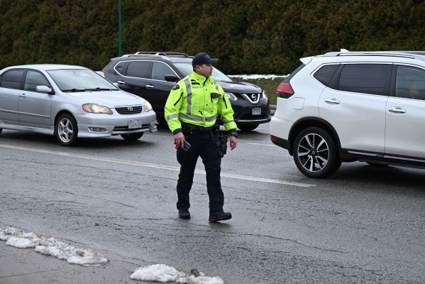 A wide photo of a police officer in a reflective jacket walking near traffic