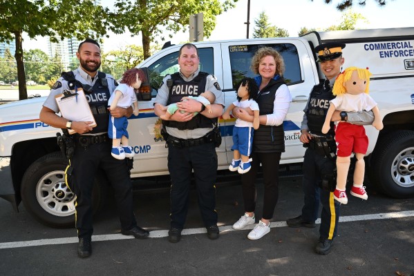 Three police officers and a BCAA employee holding dolls in front of a police truck for a car and booster seat safety initiative.