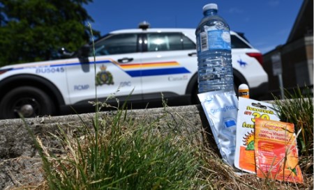 A police cruiser with a care package in the foreground, including a bottle of water, lip balm, sunscreen, and a cooling patch.
