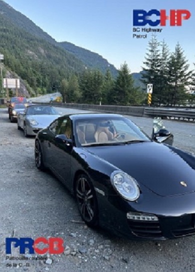 Side view of 3 stopped Porsche cars lined up on the highway shoulder with police vehicle behind them