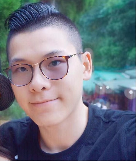 Young Asian man with black hair shaved quite short on the sides, brown eyes, wearing brown rimmed glasses, a t-shirt..