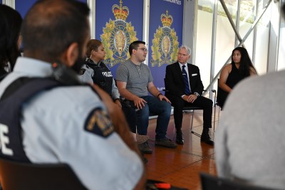 •&#9;Une image montrant le dos d'un policier et plusieurs personnes en tenue civile assises sur des chaises en cercle dans un bâtiment portant les logos de la GRC.