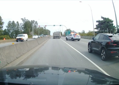 Rear view of dump truck crossing over solid line from left to right, with marked police vehicle behind it pulling it over