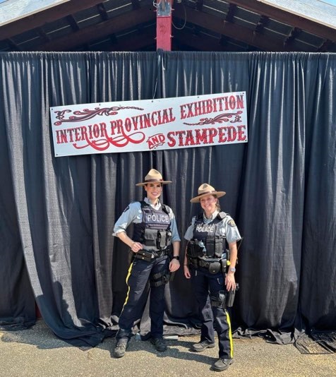 Les gendarmes Valotaire et Taylor, agentes de la GRC, posent devant une bannière de l’Exposition provinciale intérieure.