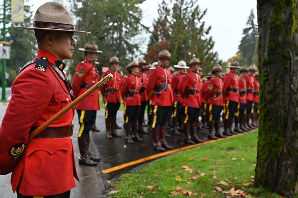 An RCMP officer in Red Serge stands beside a group of officers in also Red Serge outdoors in the rain  