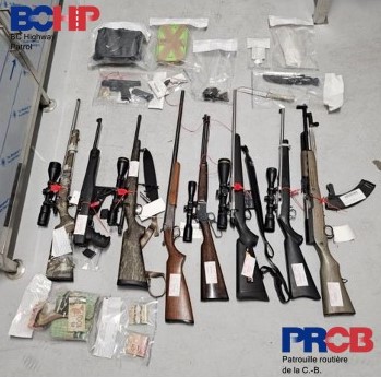 De nombreuses armes à feu, de l’argent emballé et divers objets sont placés devant un fond gris.