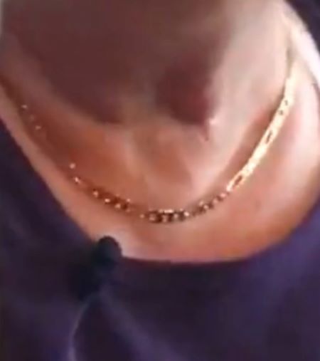 A gold necklace on the neckline of a woman wearing a purple shirt. 