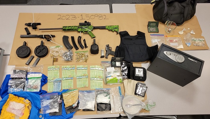 Photo of firearms, cash in $20 dollar bills, bags of suspected drugs, body armor displayed on table