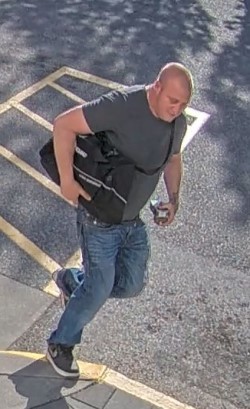 Photo of suspect 2 wearing a grey t-shirt, blue jeans, black/white runners and carrying a black bag.