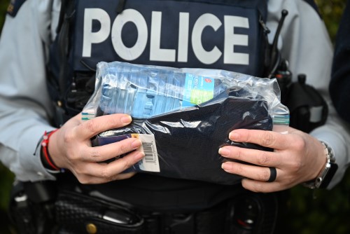 A police officer in uniform with hands visible holds a plastic bag with a number of items inside including gloves and a water bottle