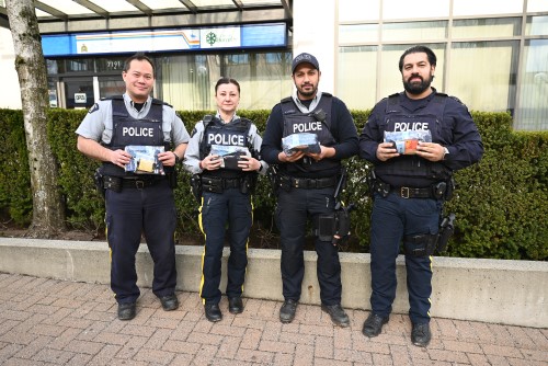 Four police officers in uniform stand outdoors holding plastic bags filled with cold weather items such as gloves and socks