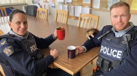 Two police officers sit at a table for coffee break. One is holding a red mug, the other, a black one. 