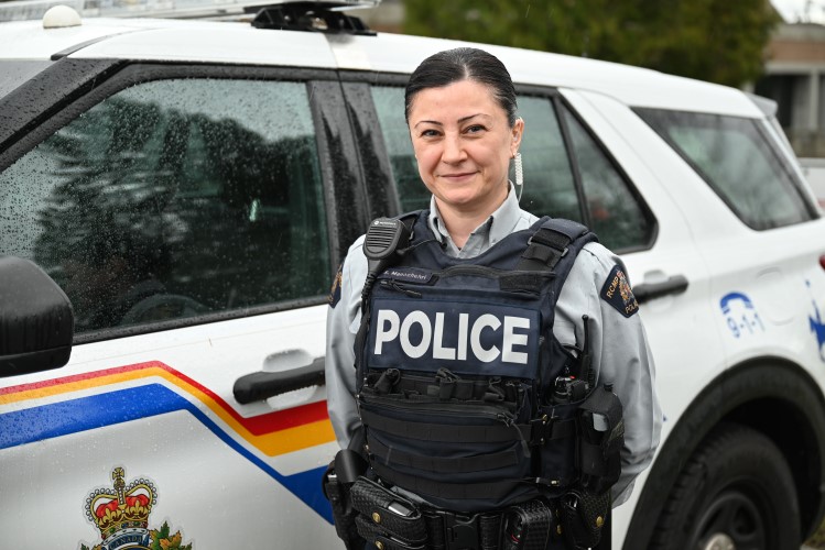 Cst. Sahar Manochehri smiles outdoors beside a police SUV on a rainy day