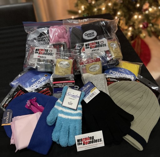 A warming the homeless package with various items including a toque and gloves beside a Christmas tree